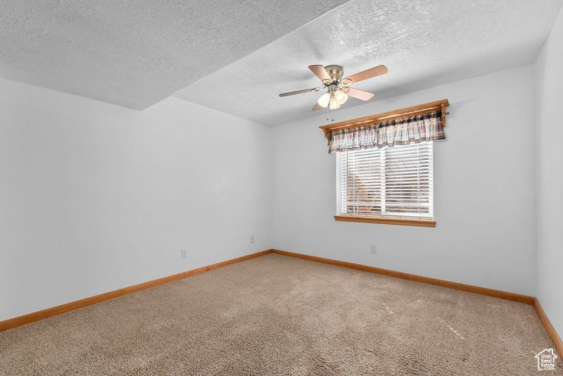 Empty room with ceiling fan, a textured ceiling, and carpet