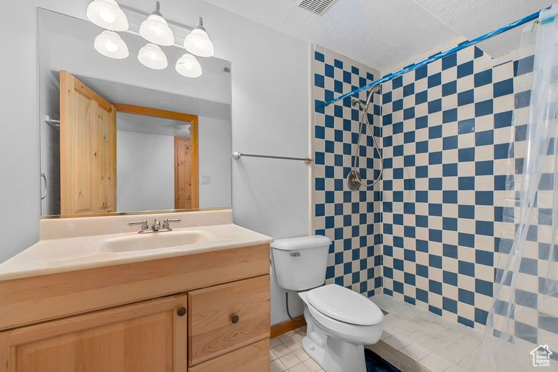 Bathroom featuring curtained shower, tile flooring, toilet, vanity with extensive cabinet space, and a textured ceiling