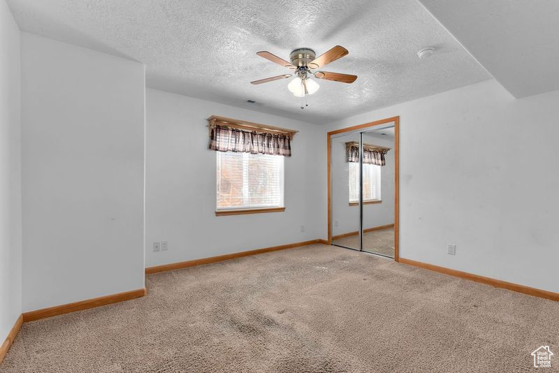 Unfurnished room featuring light carpet, a textured ceiling, and ceiling fan