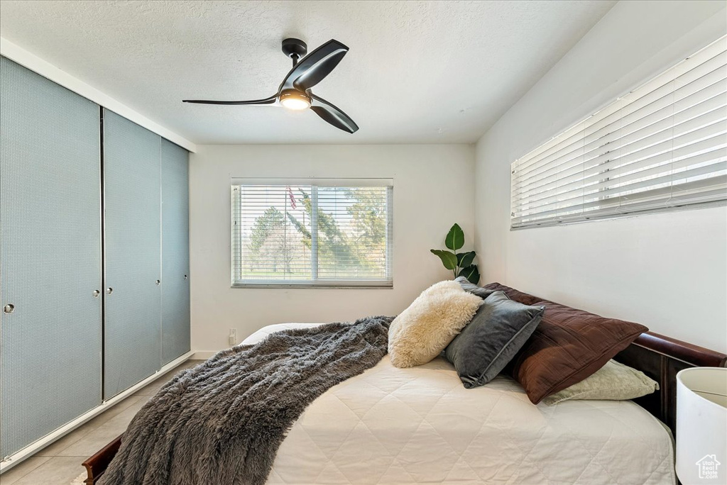 Tiled bedroom with ceiling fan, a textured ceiling, and a closet