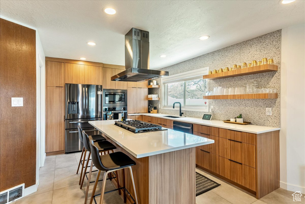 Kitchen featuring appliances with stainless steel finishes, a center island, a breakfast bar, backsplash, and island exhaust hood