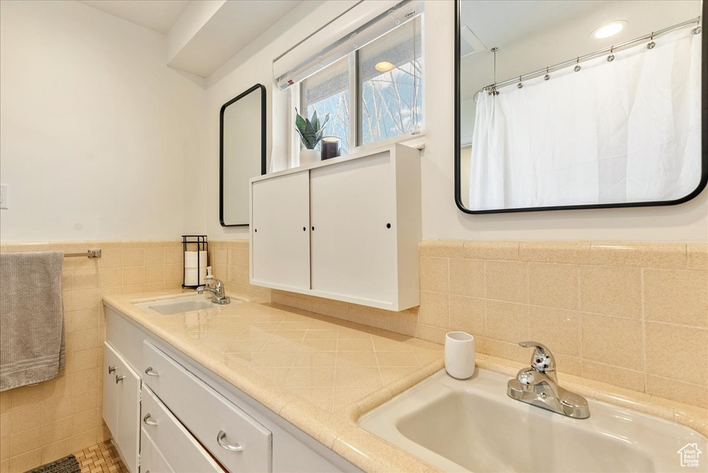 Bathroom with double vanity, tile walls, and tasteful backsplash