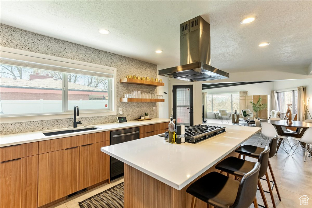 Kitchen with light tile flooring, a kitchen island, a kitchen breakfast bar, sink, and island exhaust hood