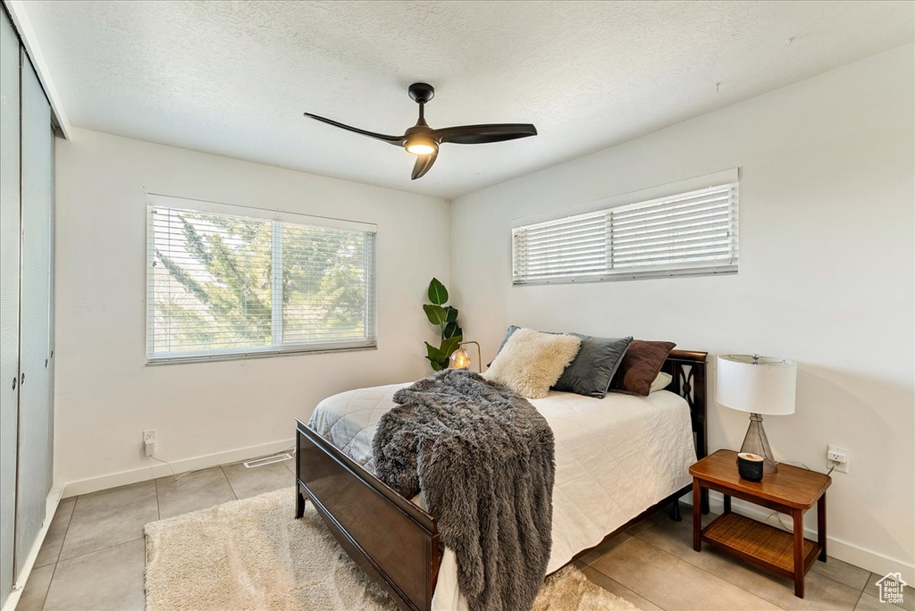 Bedroom featuring ceiling fan, a closet, light tile floors, and a textured ceiling