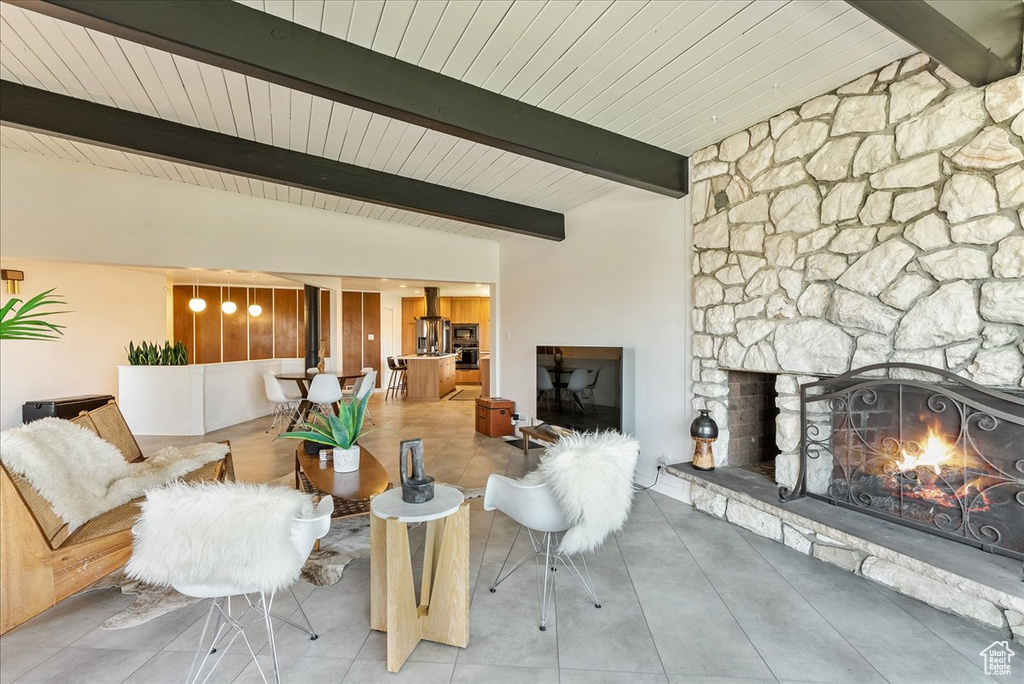 Tiled living room with lofted ceiling with beams and a stone fireplace