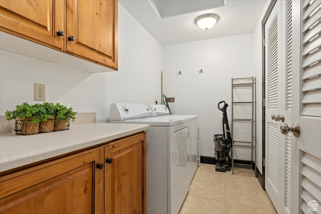 Clothes washing area featuring light tile flooring, cabinets, and washer and dryer