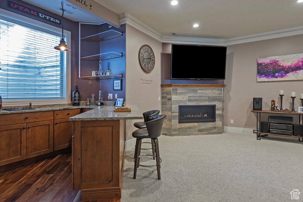 Bar with ornamental molding, light stone counters, a tile fireplace, and hanging light fixtures