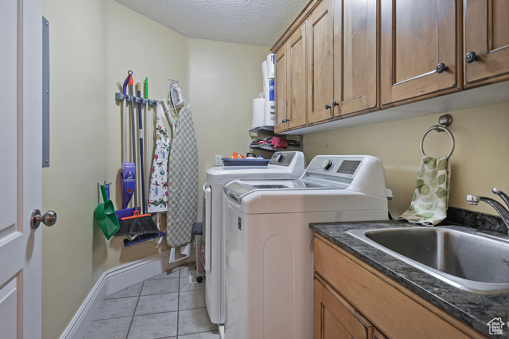 Washroom with washing machine and dryer, sink, light tile flooring, a textured ceiling, and cabinets