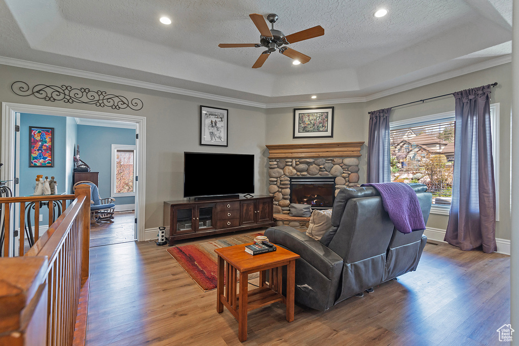 Living room with ceiling fan, a raised ceiling, a textured ceiling, a stone fireplace, and hardwood / wood-style flooring