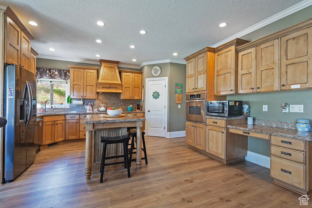 Kitchen featuring appliances with stainless steel finishes, dark stone counters, a breakfast bar, premium range hood, and dark hardwood / wood-style flooring