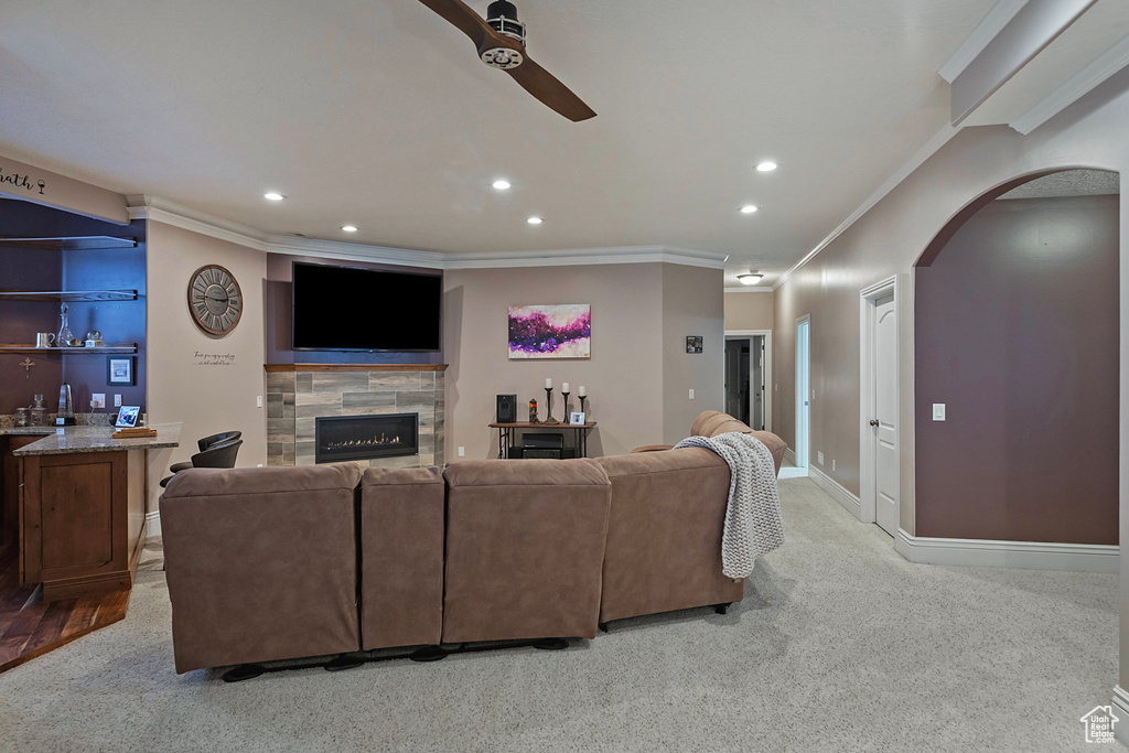 Living room featuring a tiled fireplace, ceiling fan, crown molding, and light carpet