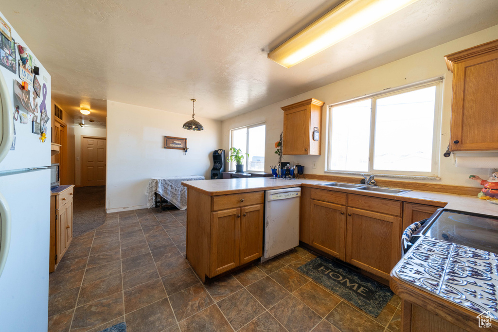 Kitchen featuring dark tile floors, decorative light fixtures, white appliances, kitchen peninsula, and sink