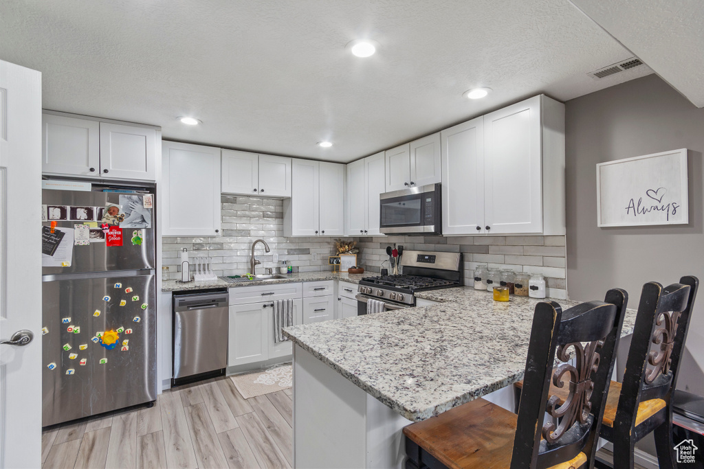 Kitchen with appliances with stainless steel finishes, light stone counters, a kitchen breakfast bar, kitchen peninsula, and light hardwood / wood-style flooring