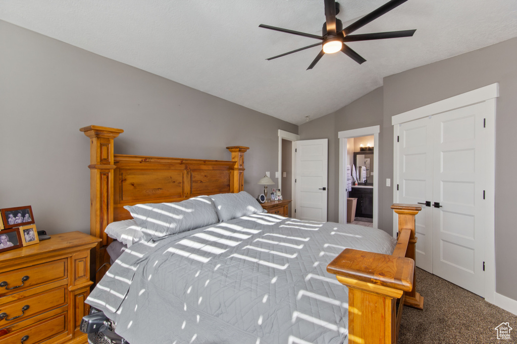 Bedroom featuring ceiling fan, dark carpet, ensuite bath, and vaulted ceiling