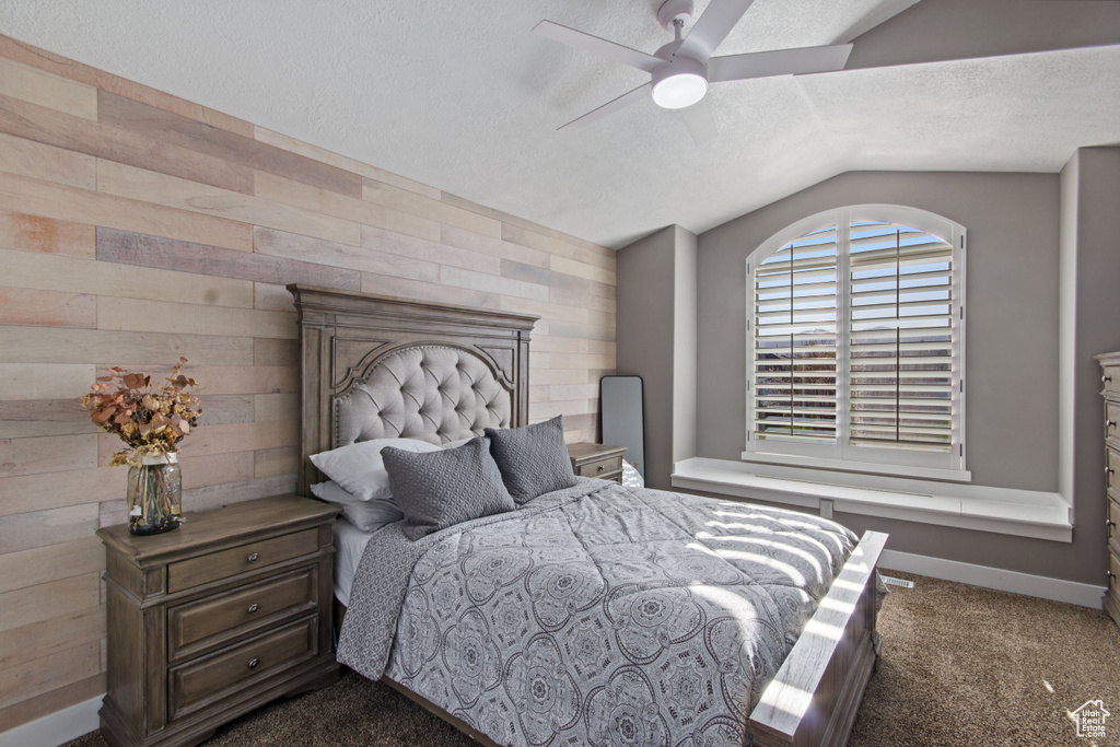 Bedroom with wooden walls, dark carpet, ceiling fan, a textured ceiling, and lofted ceiling