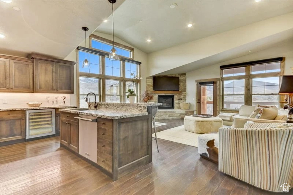 Kitchen with light stone countertops, decorative light fixtures, a stone fireplace, dark wood-type flooring, and wine cooler
