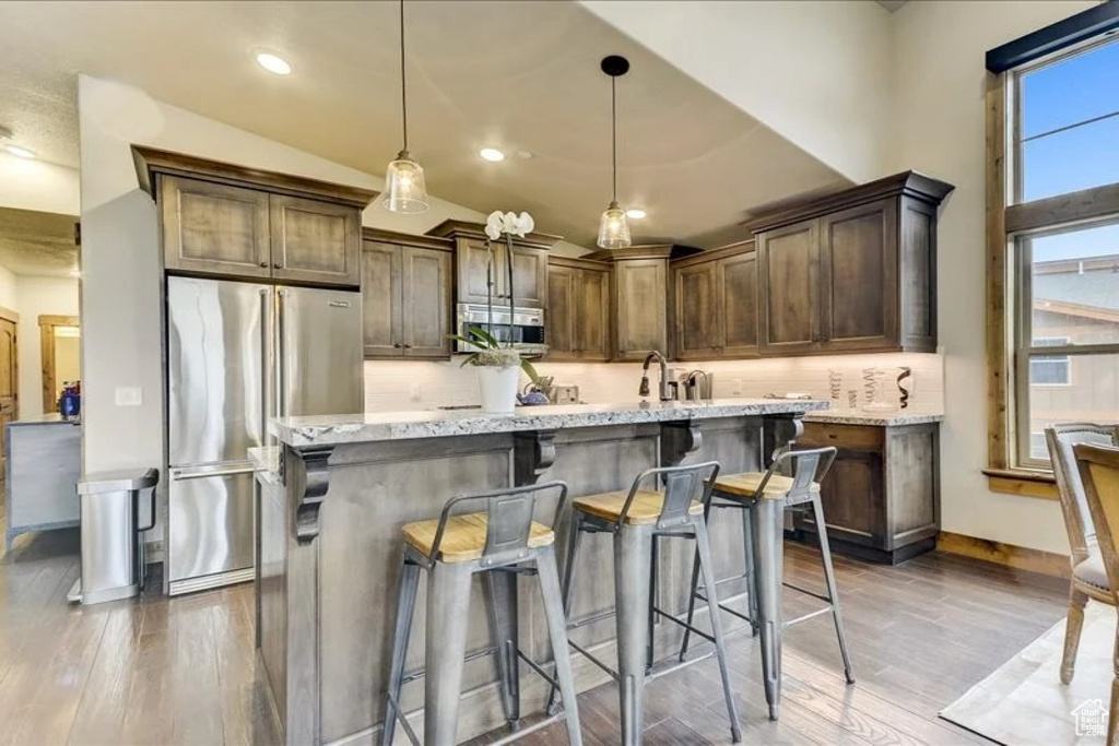 Kitchen featuring tasteful backsplash, pendant lighting, wood-type flooring, and a kitchen bar