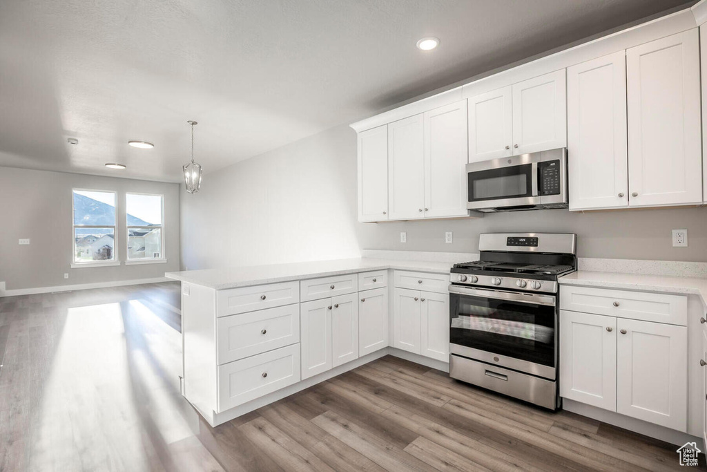 Kitchen featuring stainless steel appliances, white cabinets, pendant lighting, and light hardwood / wood-style flooring