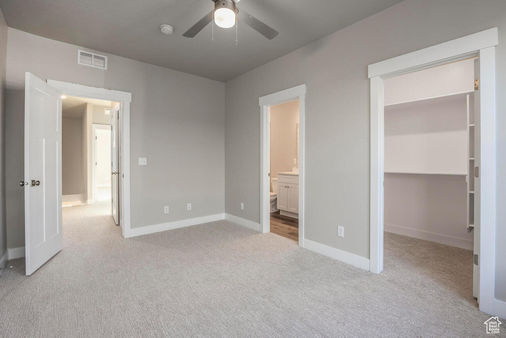 Unfurnished bedroom featuring ceiling fan, ensuite bathroom, light carpet, and a spacious closet