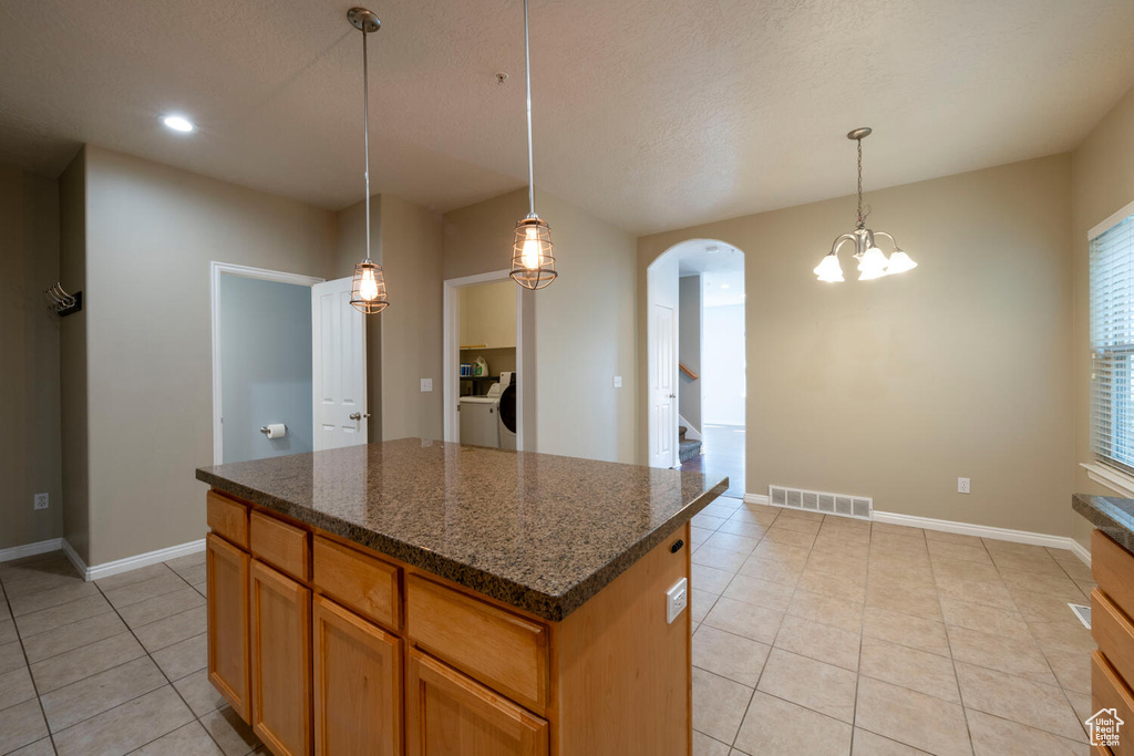Kitchen with washing machine and dryer, a chandelier, pendant lighting, a center island, and light tile floors