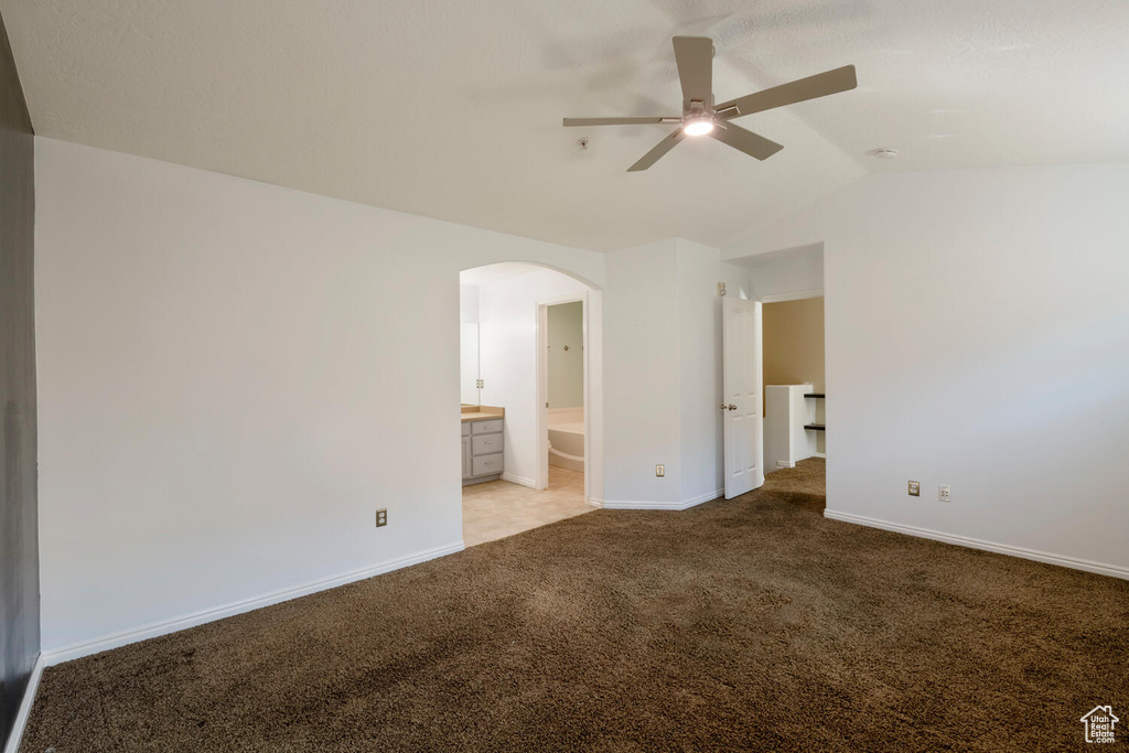 Unfurnished bedroom with connected bathroom, light carpet, ceiling fan, and vaulted ceiling