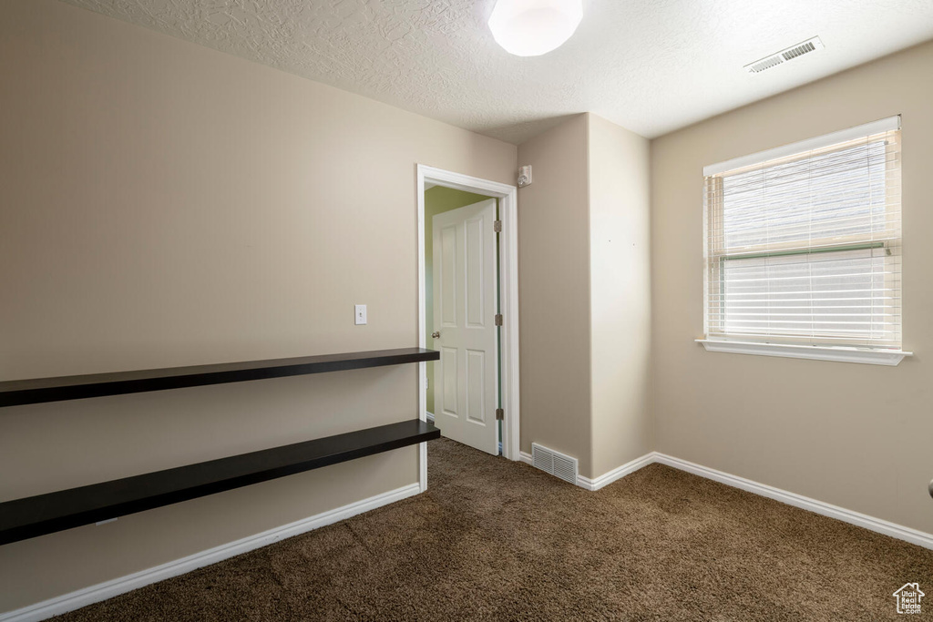 Unfurnished bedroom featuring a textured ceiling and dark colored carpet