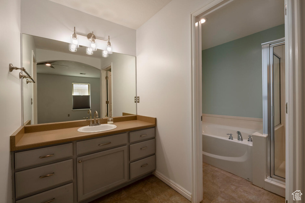 Bathroom featuring ceiling fan, vanity with extensive cabinet space, shower with separate bathtub, and tile flooring