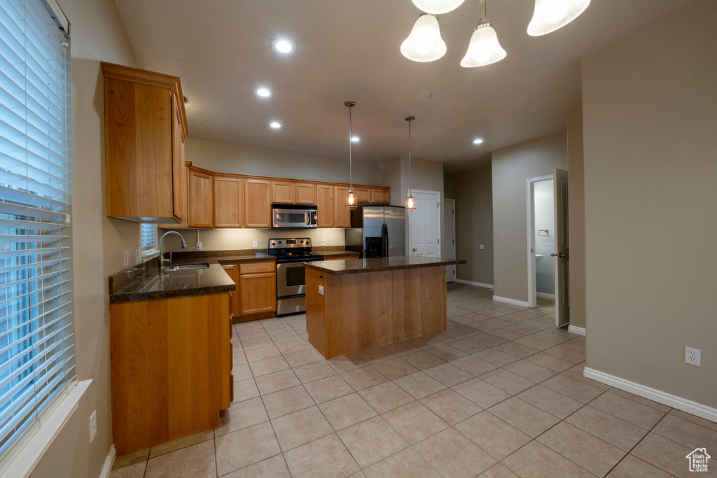 Kitchen with decorative light fixtures, appliances with stainless steel finishes, dark stone countertops, a center island, and light tile floors