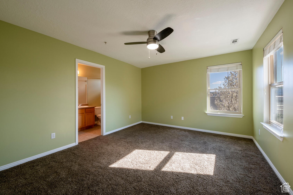 Unfurnished bedroom featuring dark colored carpet, ceiling fan, and ensuite bathroom