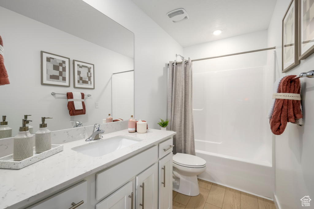 Full bathroom featuring hardwood / wood-style flooring, shower / bathtub combination with curtain, toilet, and vanity