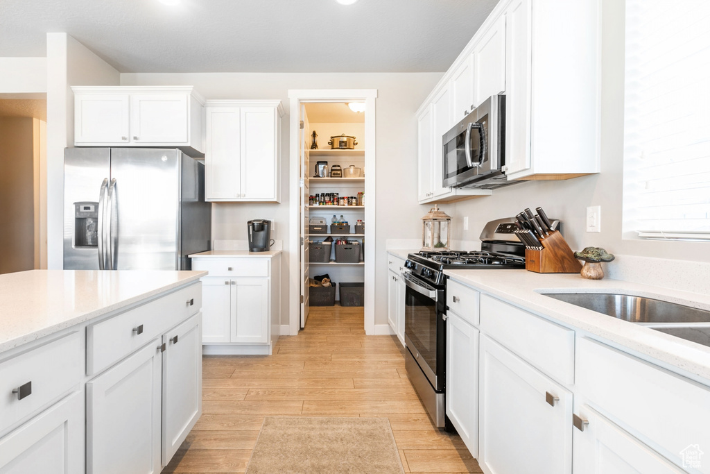 Kitchen featuring appliances with stainless steel finishes, light hardwood / wood-style floors, light stone counters, and white cabinets