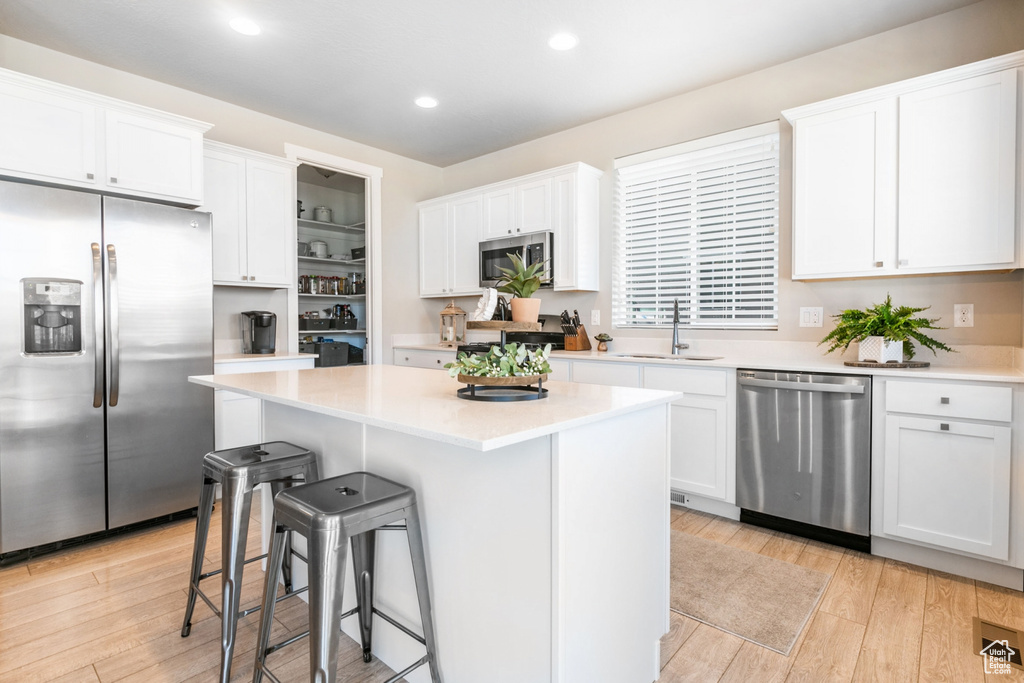Kitchen featuring light hardwood / wood-style flooring, stainless steel appliances, white cabinetry, and a kitchen island