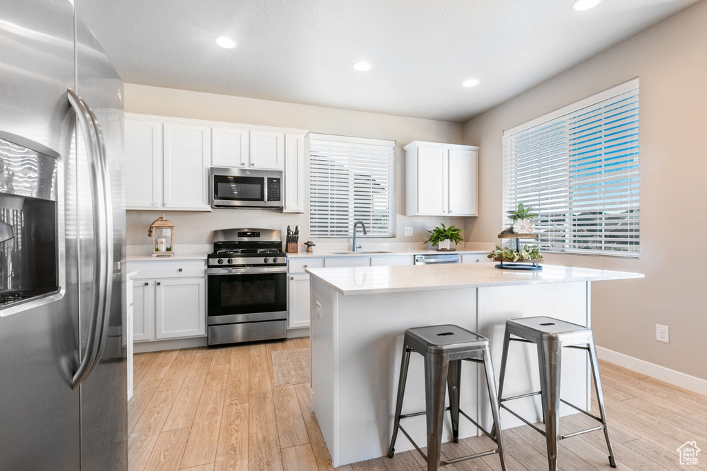 Kitchen featuring a kitchen island, stainless steel appliances, white cabinetry, and light hardwood / wood-style flooring