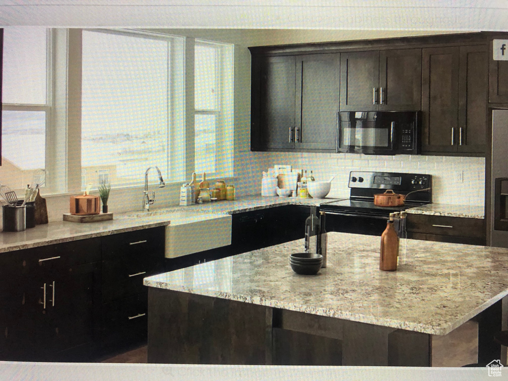 Kitchen with light stone counters, tasteful backsplash, stainless steel fridge, electric range, and a center island with sink
