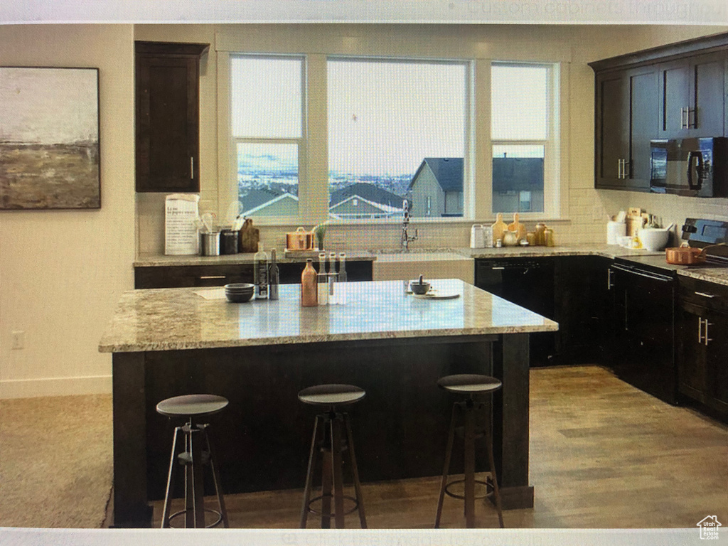 Kitchen featuring a center island, a kitchen breakfast bar, black appliances, and light stone countertops