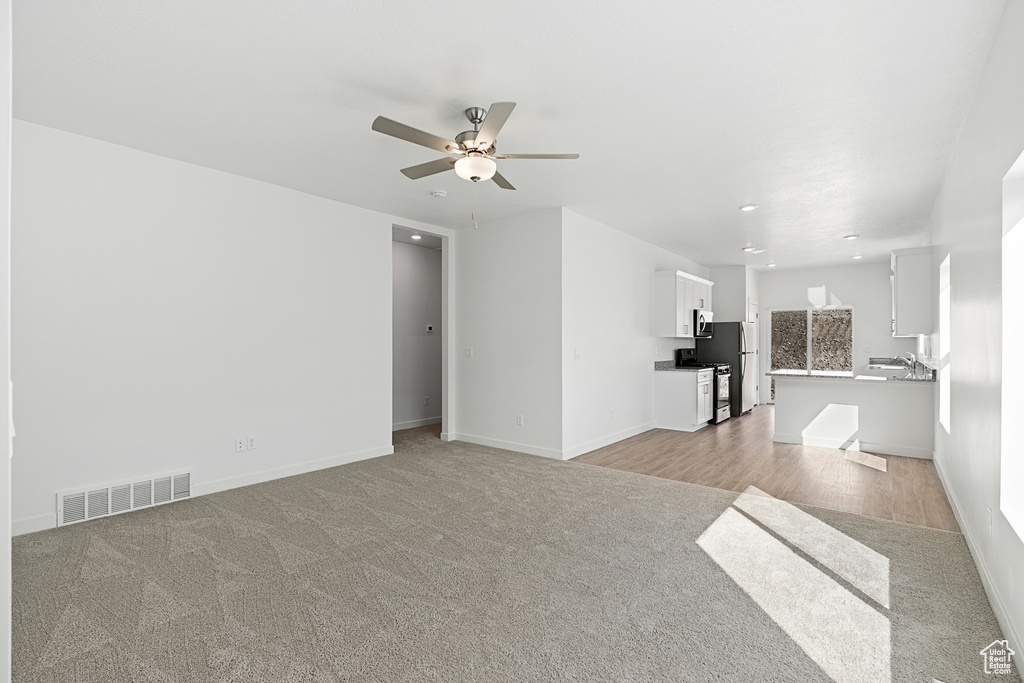 Unfurnished living room featuring ceiling fan and light carpet