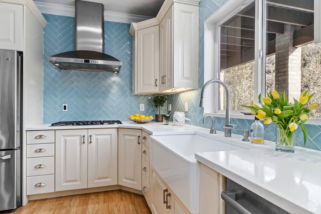 Kitchen with light wood-type flooring, crown molding, backsplash, wall chimney range hood, and stainless steel fridge