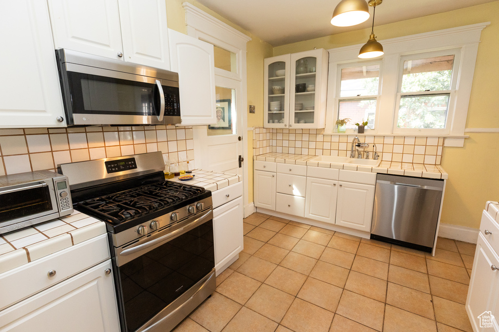 Kitchen featuring tasteful backsplash, white cabinets, stainless steel appliances, tile countertops, and sink
