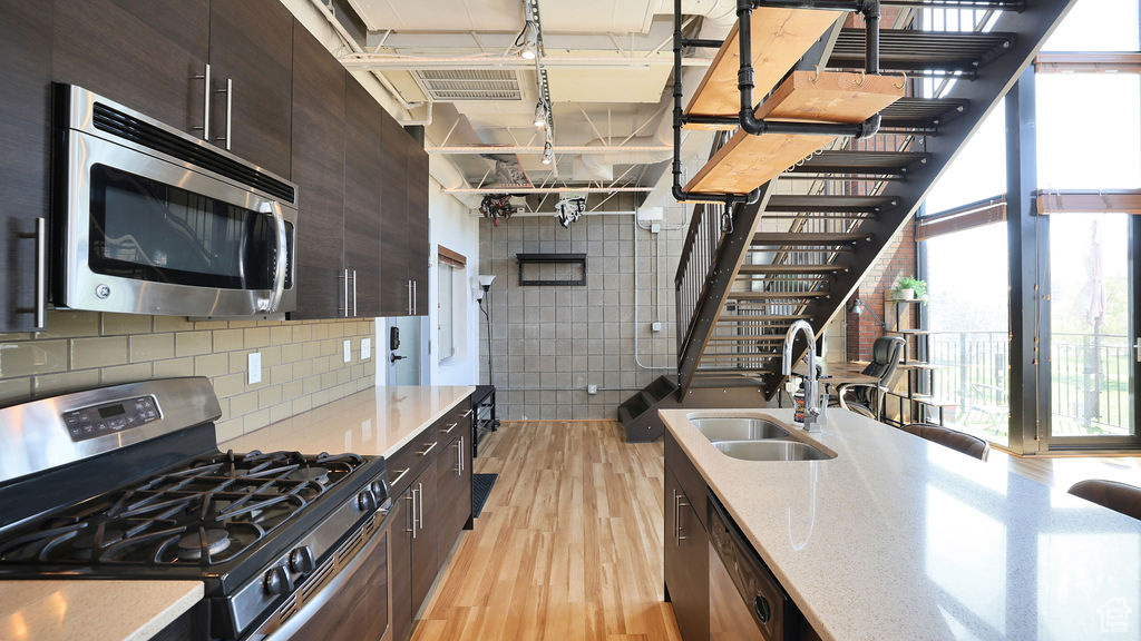 Kitchen with dark brown cabinetry, light stone counters, stainless steel appliances, light wood-type flooring, and sink