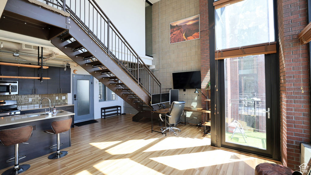 Interior space featuring brick wall, light hardwood / wood-style flooring, sink, and a towering ceiling