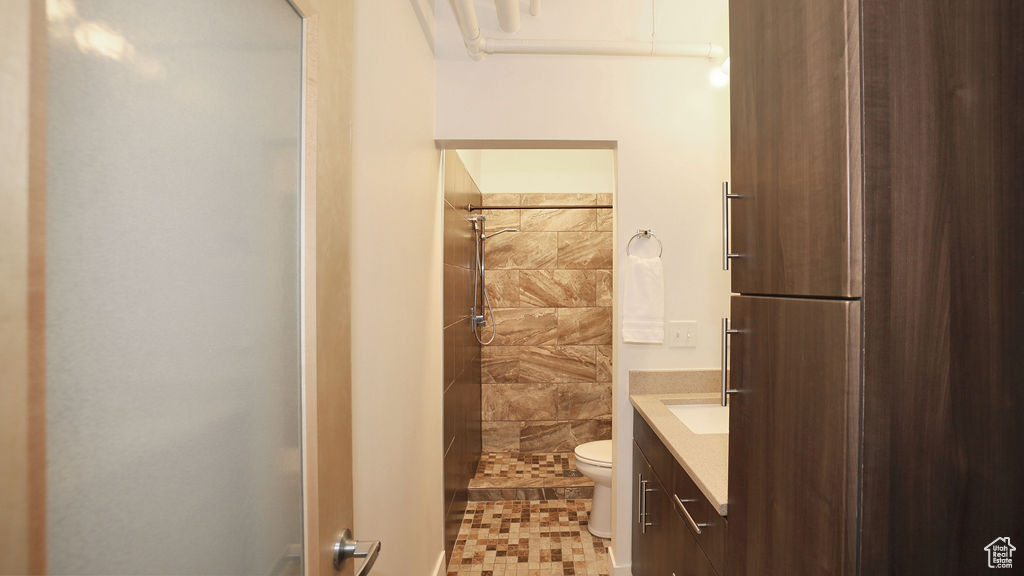 Bathroom featuring tile floors, toilet, tiled shower, and vanity
