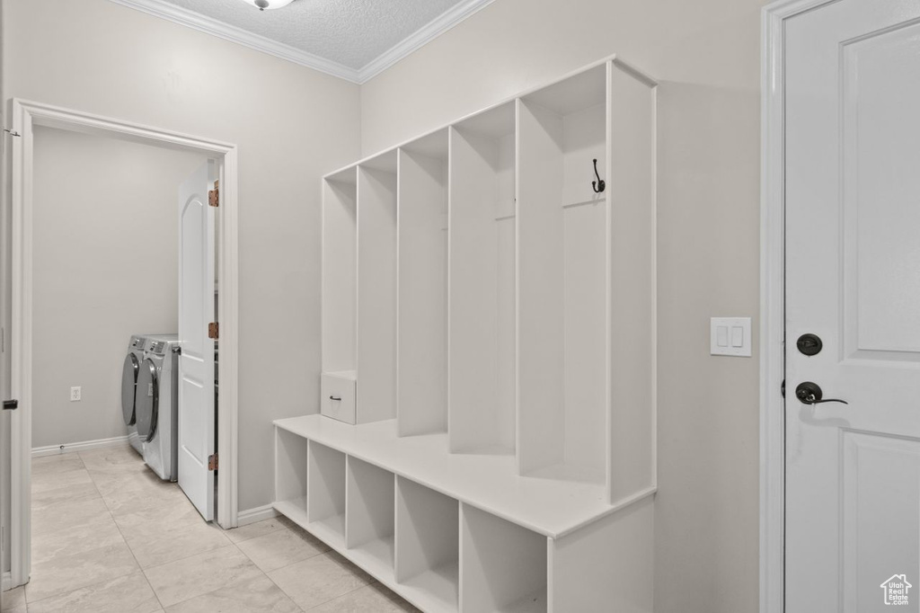 Mudroom featuring a textured ceiling, light tile floors, washer and dryer, and crown molding
