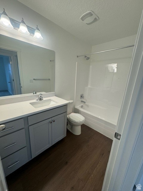 Full bathroom with hardwood / wood-style flooring, toilet, vanity, shower / tub combination, and a textured ceiling