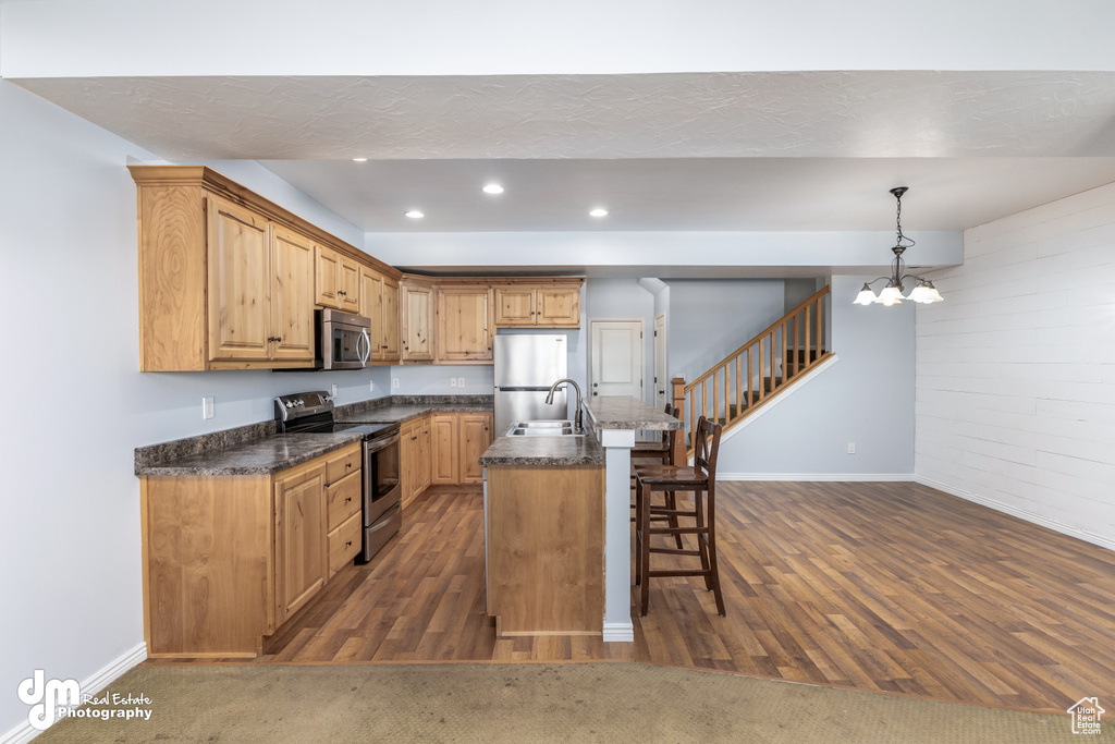Kitchen featuring decorative light fixtures, dark hardwood / wood-style flooring, appliances with stainless steel finishes, and an island with sink