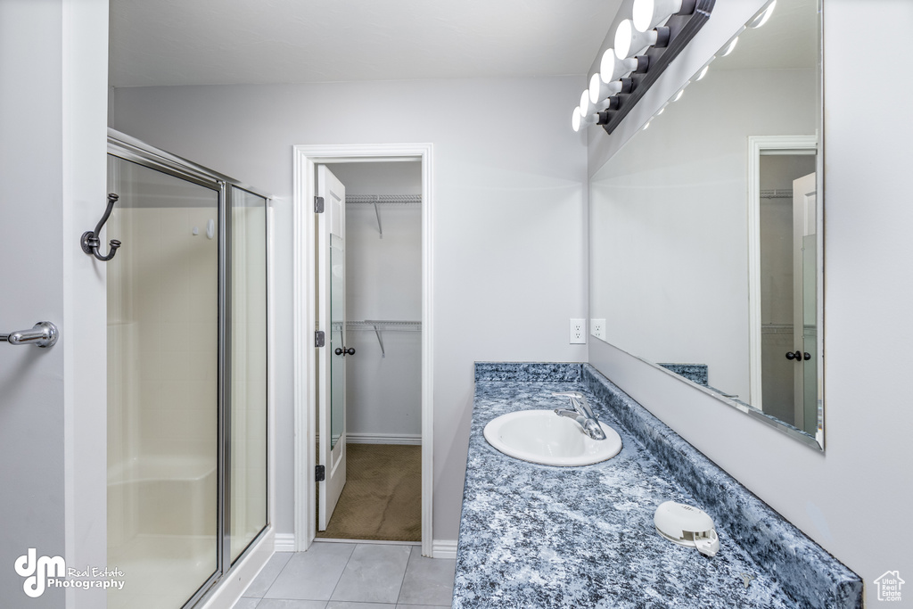 Bathroom featuring a shower with shower door, vanity with extensive cabinet space, and tile flooring