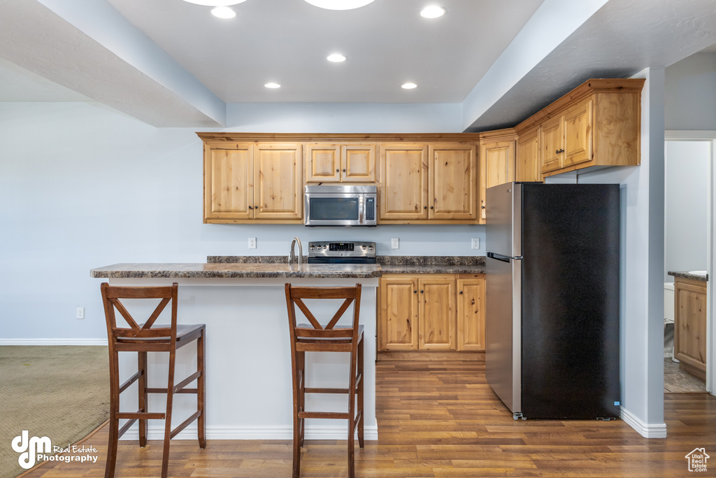 Kitchen featuring hardwood / wood-style floors, a kitchen bar, stainless steel appliances, and dark stone counters
