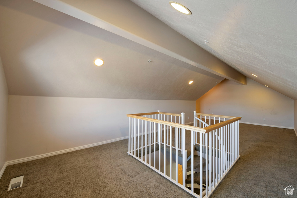 Additional living space featuring lofted ceiling with beams, dark carpet, and a textured ceiling