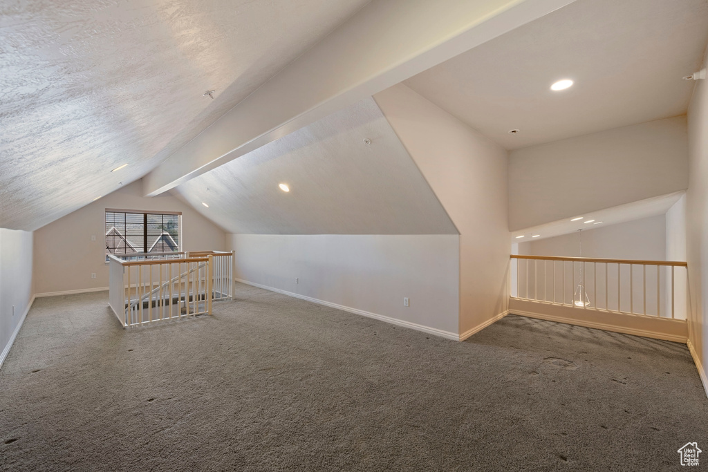 Bonus room featuring lofted ceiling with beams, a textured ceiling, and dark colored carpet