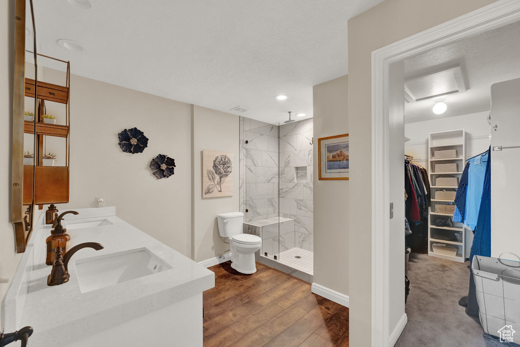 Bathroom with dual bowl vanity, wood-type flooring, tiled shower, and toilet