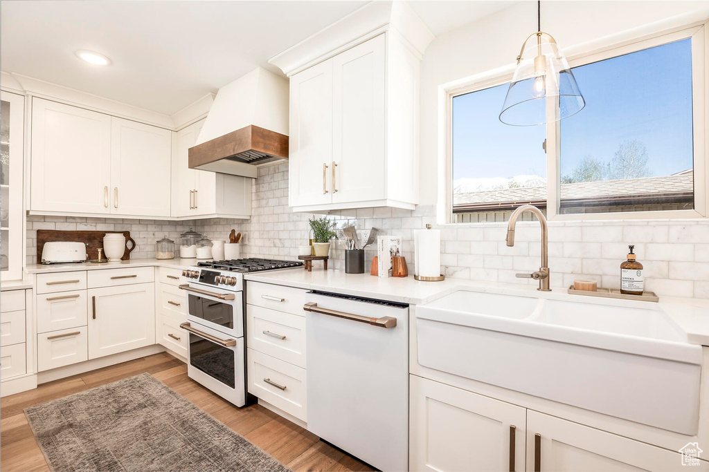 Kitchen featuring premium range hood, light wood-type flooring, tasteful backsplash, and white appliances